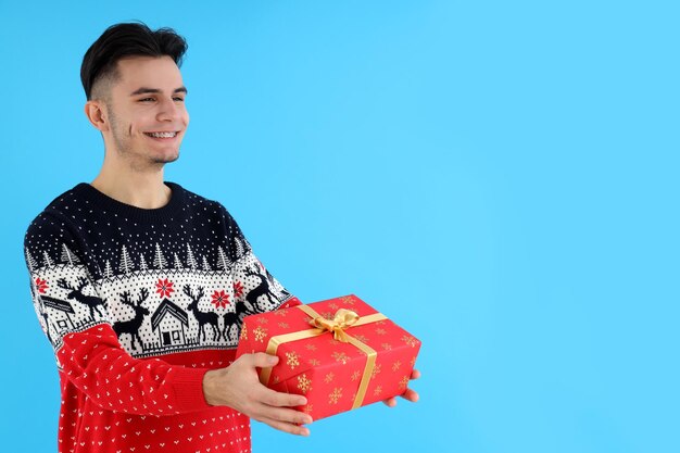 Chico atractivo con regalo de Navidad sobre fondo azul.