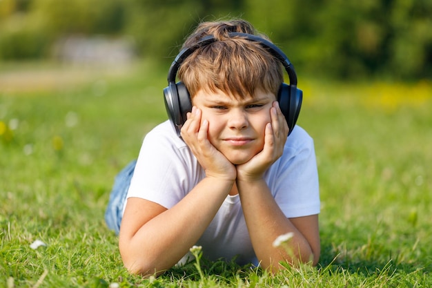 Chico con auriculares escuchando música tumbado en el césped en el parque