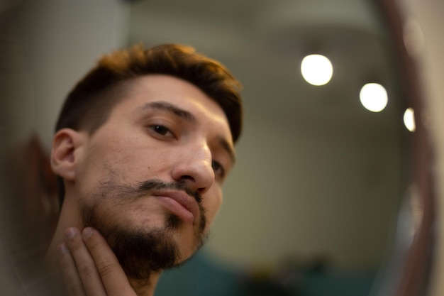 Un chico con barba irregular se mira en el espejo.