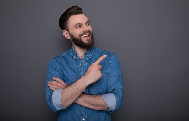 Chico barbudo sonriente feliz y emocionado sorprendido está apuntando a algo de publicidad en el espacio de la copia