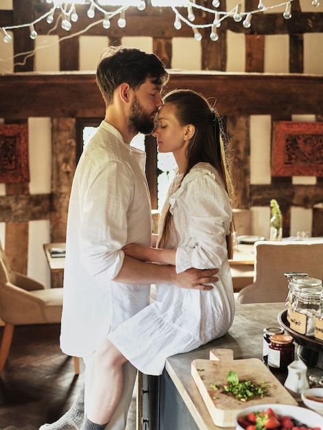 Foto el chico besa a la chica que está sentada en la mesa de la cocina, el concepto de romance,