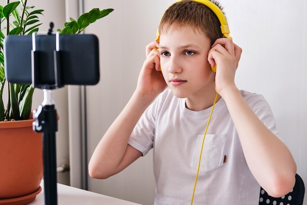 Chico blogger en auriculares amarillos hablando con seguidores Adolescente transmisión en vivo mirando a la pantalla del teléfono inteligente