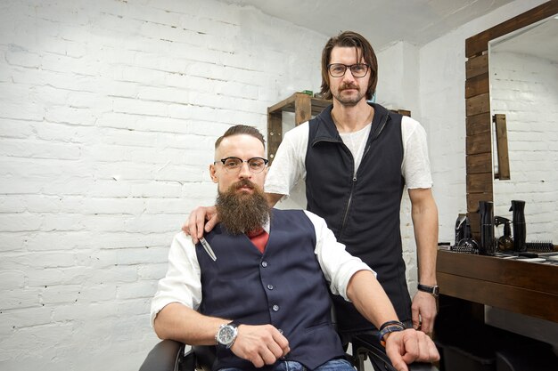 Foto chico brutal en la moderna peluquería. peluquero hace peinado a un hombre con una larga barba. maestro peluquero hace peinado con tijeras y peine