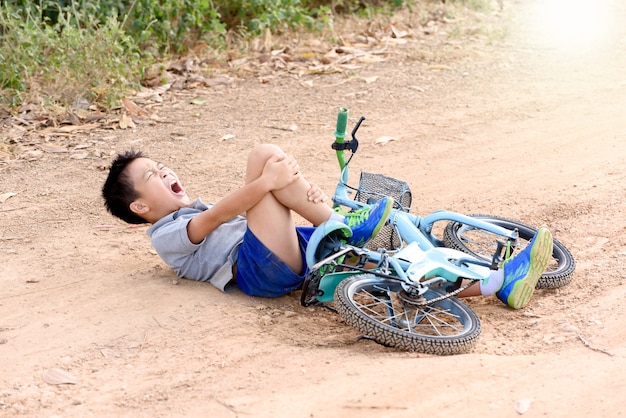 Chico caer de la bicicleta durante el paseo en la carretera