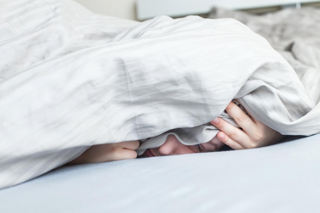 Chico en la cama por la mañana. el niño miente y se cubre la cara con una manta