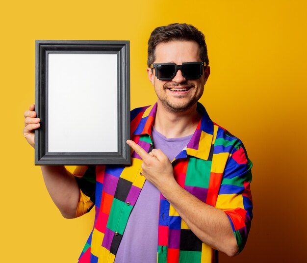 Chico en camisa de los 90 y gafas de sol con marco de fotos