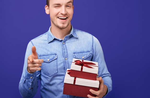 Chico con una camisa azul de pie con dos regalos y puntos con el dedo índice recto