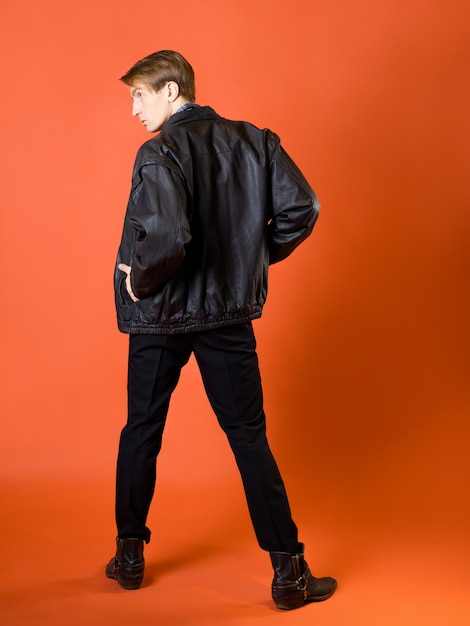 Un chico con una camisa a cuadros casual y una chaqueta de cuero foto de estudio sobre un fondo naranja