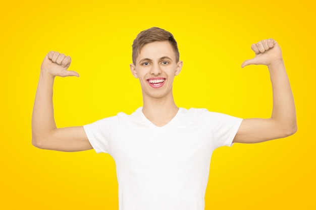 Un chico con una camiseta blanca con las manos en alto en el estudio en un amarillo, aislar