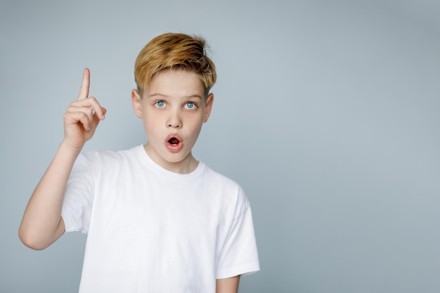 El chico de la camiseta blanca se sorprende de que tenga una idea eureka levantó el dedo índice aislado en un fondo gris