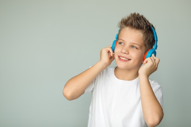 Chico en una camiseta escucha música con auriculares inalámbricos azules y sonríe