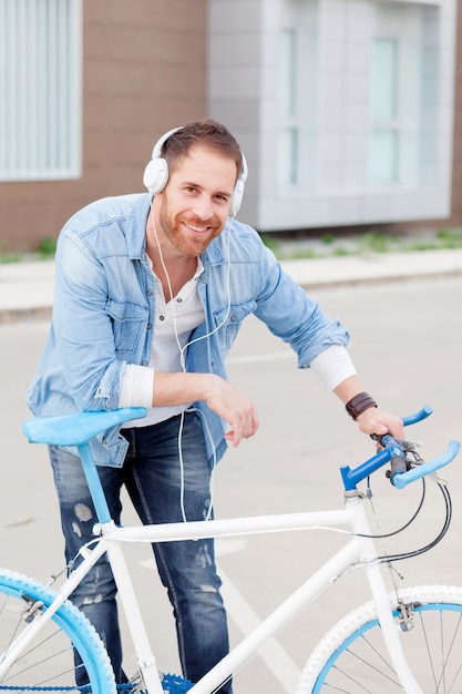 Chico casual junto a una bicicleta vintage escuchando música.
