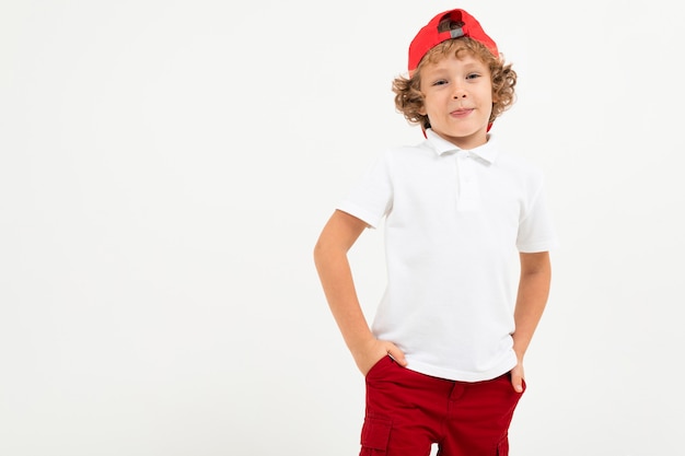 Foto chico caucásico en camiseta blanca, gorra roja, pantalones cortos rojos sonrisas aisladas en blanco