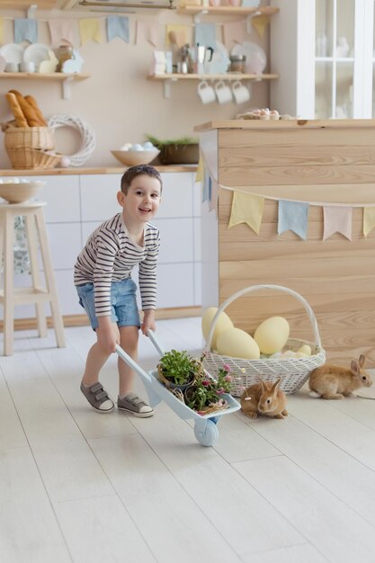 Chico caucásico con lindo conejito en un interior de cocina claro con decoraciones de Pascua