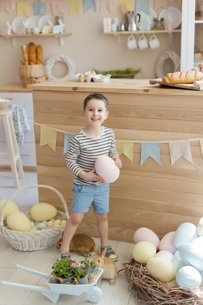 Chico caucásico con lindo conejito en un interior de cocina claro con decoraciones de Pascua