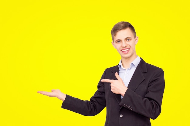 El chico de la chaqueta y la camisa azul anuncia el producto aislado sobre un fondo amarillo