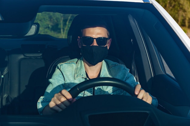 Chico con una chaqueta de mezclilla y gafas negras con una máscara en la cara conduciendo un coche