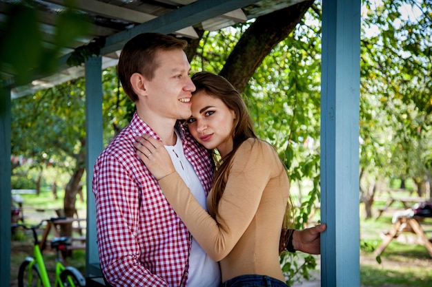 El chico con una chica se abraza cerca de una casa de madera.