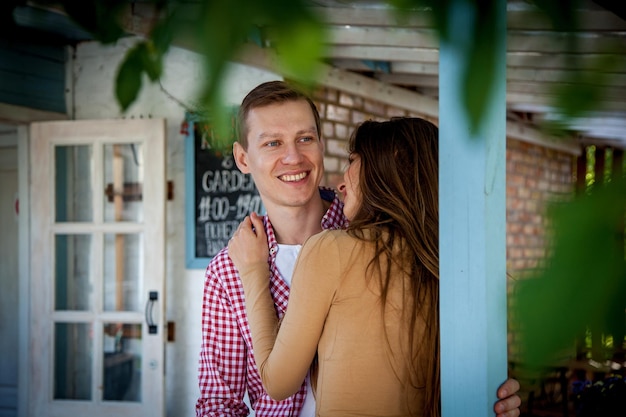 El chico con una chica se abraza cerca de una casa de madera.