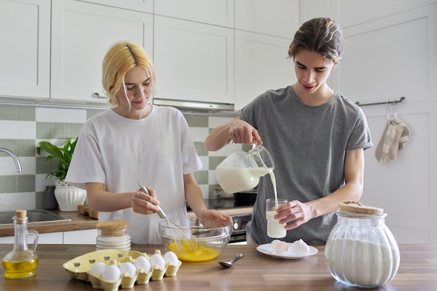 Chico y chica adolescentes cocinando panqueques en la cocina juntos