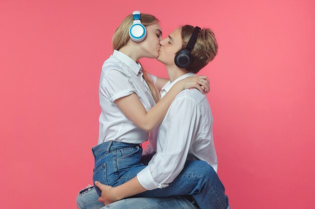 Foto chico con una chica en auriculares besos sobre fondo rosa