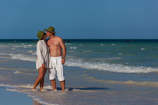 Chico y chica besándose en la playa al borde del surf