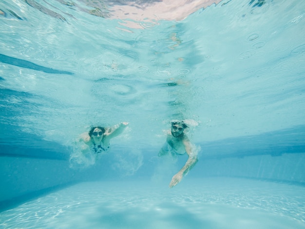 Chico y chica buceando en piscina