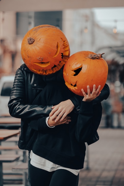 Un chico y una chica con cabezas de calabaza posando en la calle.