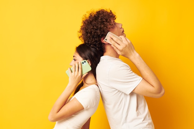 Un chico con una chica con camisetas blancas hablando por teléfono con fondo amarillo
