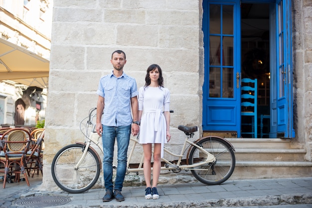 Chico y chica cerca de bicicleta tándem, paredes y puerta vintage