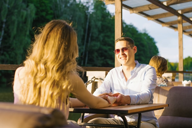 Un chico y una chica en una cita están sentados en una mesa en un café de la calle en el lago. Son felices y sonrientes