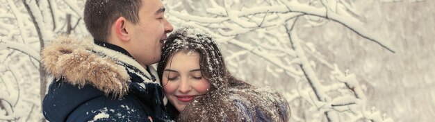 El chico y la chica descansan en el bosque de invierno Marido y mujer en la nieve Pareja joven caminando en el parque de invierno