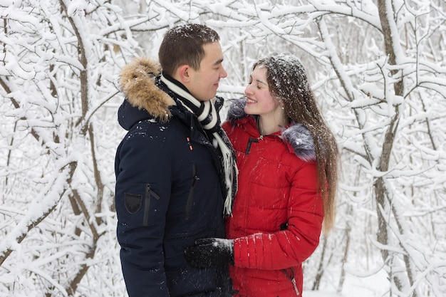 El chico y la chica descansan en el bosque de invierno Marido y mujer en la nieve Pareja joven caminando en el parque de invierno