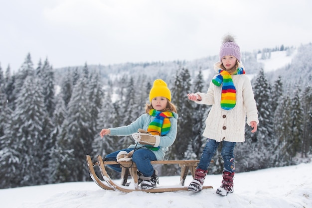 Chico y chica divertidos divirtiéndose con un trineo en invierno lindos niños jugando en una actividad de invierno de nieve