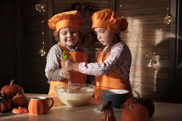 Chico y chica divertidos en trajes de chef naranja preparan pastel de calabaza. los niños se están preparando para el Día de Acción de Gracias. el concepto de unas vacaciones en familia