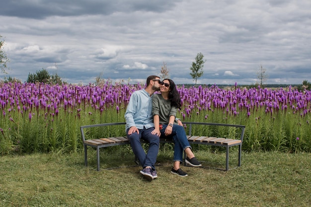 Un chico y una chica enamorados están sentados en un banco en el parque cerca de las flores.