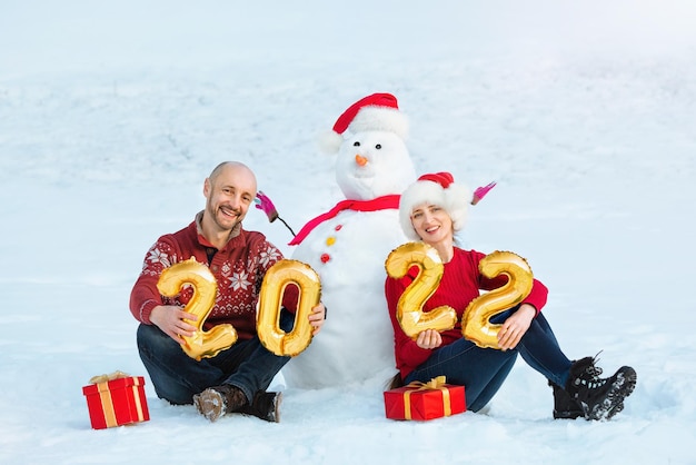 Foto un chico y una chica junto a un muñeco de nieve tienen en sus manos las figuras del próximo año nuevo