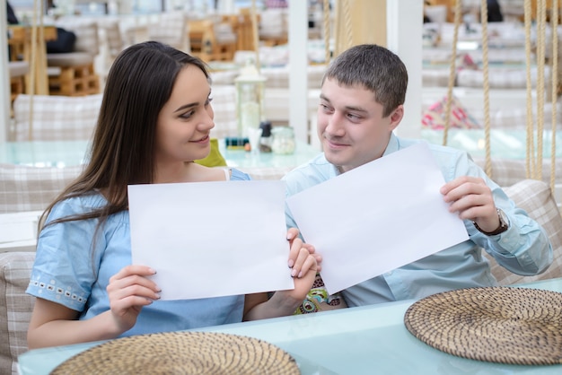 Chico y chica se miran y sostienen hojas de papel limpias