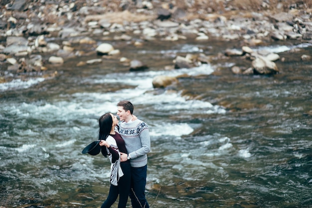 Chico y chica en suéteres calientes caminando por un río de montaña, historia de amor