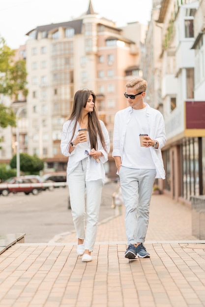 Chico con una chica vestida de blanco camina por la ciudad y bebe café