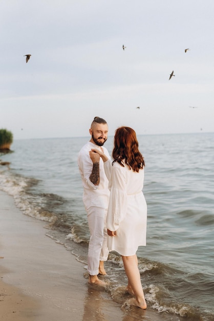 Foto un chico con una chica vestida de blanco a la orilla del mar.