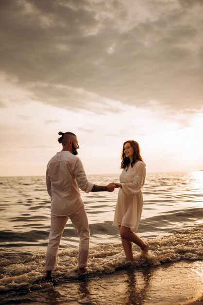 Un chico con una chica vestida de blanco a la orilla del mar.