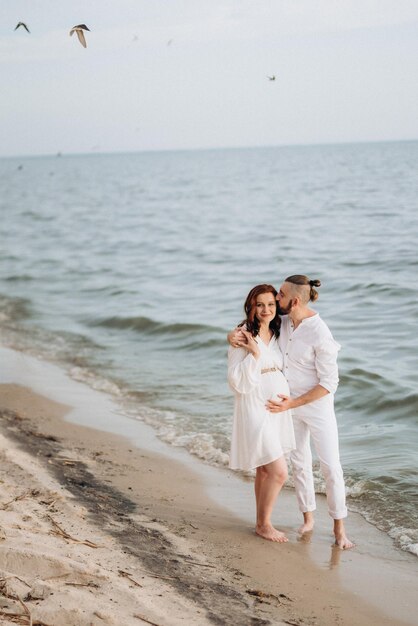 Un chico con una chica vestida de blanco a la orilla del mar.