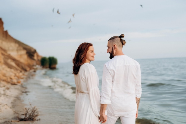 Un chico con una chica vestida de blanco a la orilla del mar.