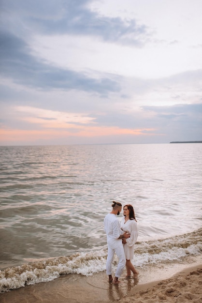 Un chico con una chica vestida de blanco a la orilla del mar.