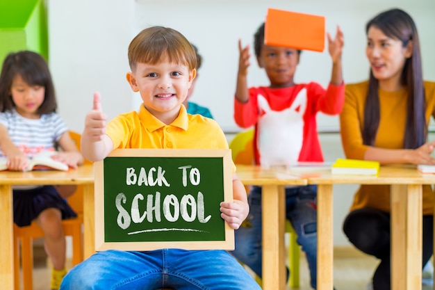 Chico chico pulgares arriba y sosteniendo la pizarra con la vuelta a la palabra de la escuela con amigos de la diversidad