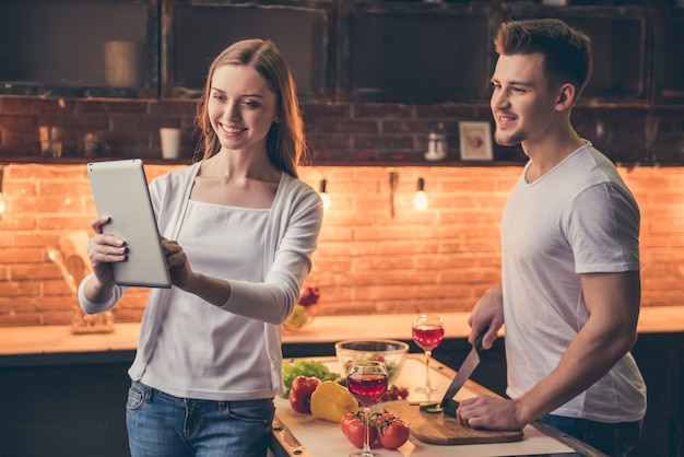 Chico en la cocina mientras su novia le está mostrando tableta.