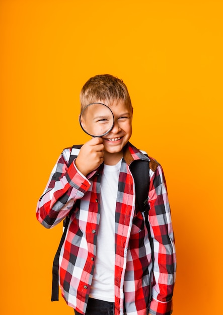 Foto chico colegial mirando a través de una lupa, agrandando su ojo sobre un fondo amarillo
