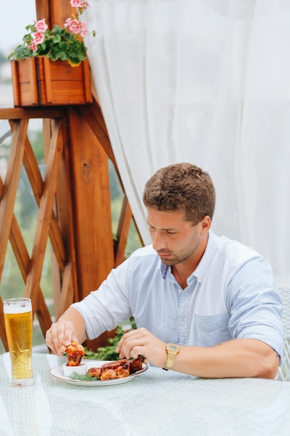 Chico come alitas de pollo a la parrilla y bebe cerveza en un restaurante