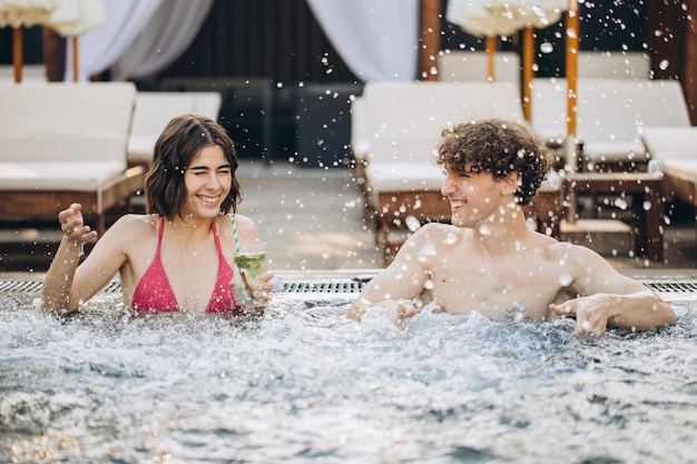 El chico coquetea con una chica en el jacuzzi Pareja relajándose en la piscina y disfrutando del verano